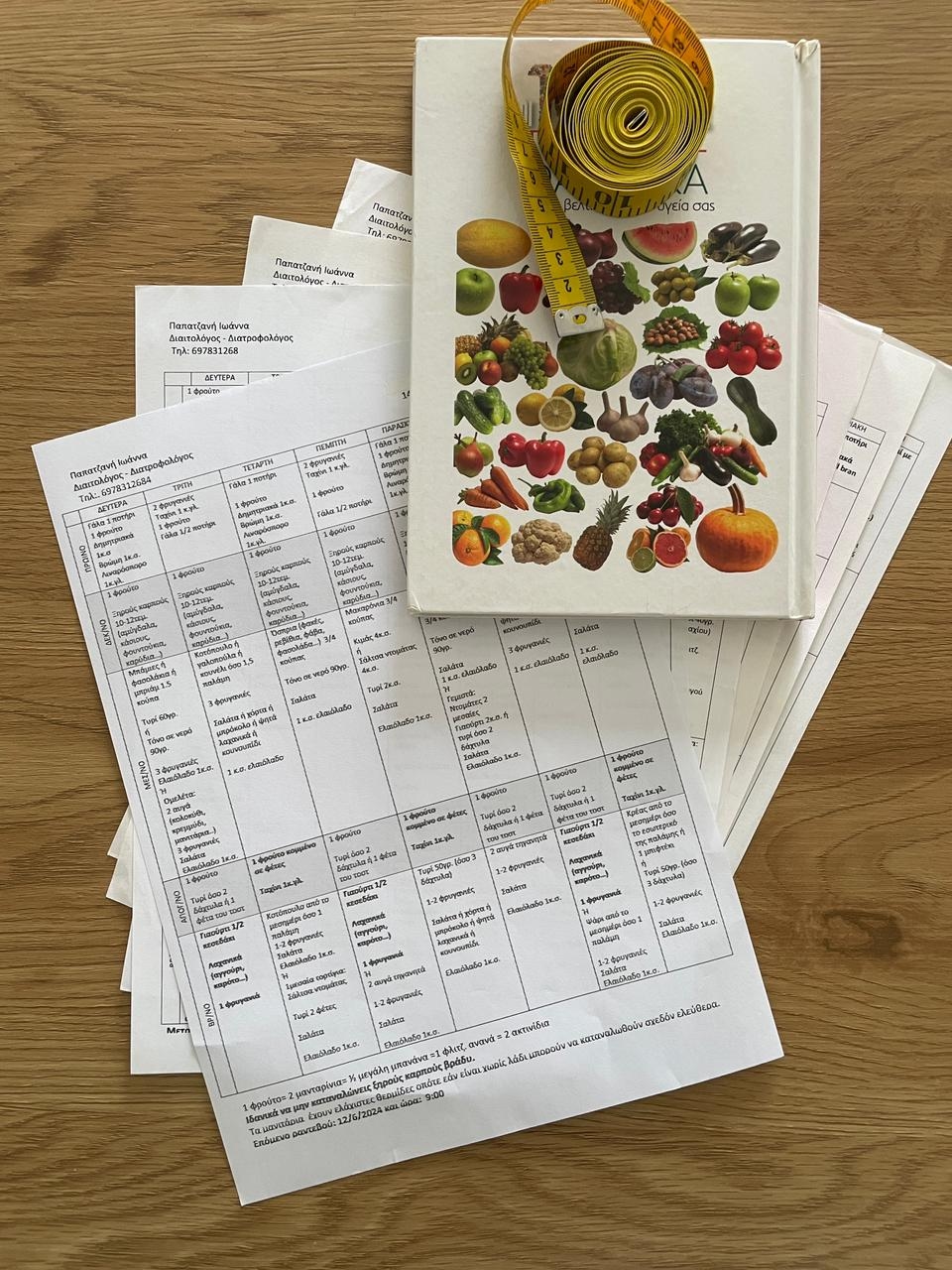 a stack of weekly meal plans on a desk, with a book on nutrition on top